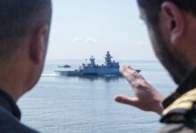 German Chancellor Olaf Scholz speaks with a serviceman as he stands aboard the frigate Mecklenburg-Vorpommern during his visit of the German Navy during a military maneuver in the Baltic Sea near Rostock-Warnemünde, northeastern Germany