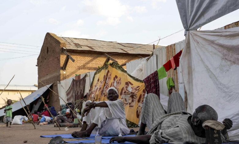 Men sit and lie outside tents and shelters pitched at the Hasahisa secondary school on July 10, 2023, which has been made into a make-shift camp to house the internally displaced fleeing violence in war-torn Sudan