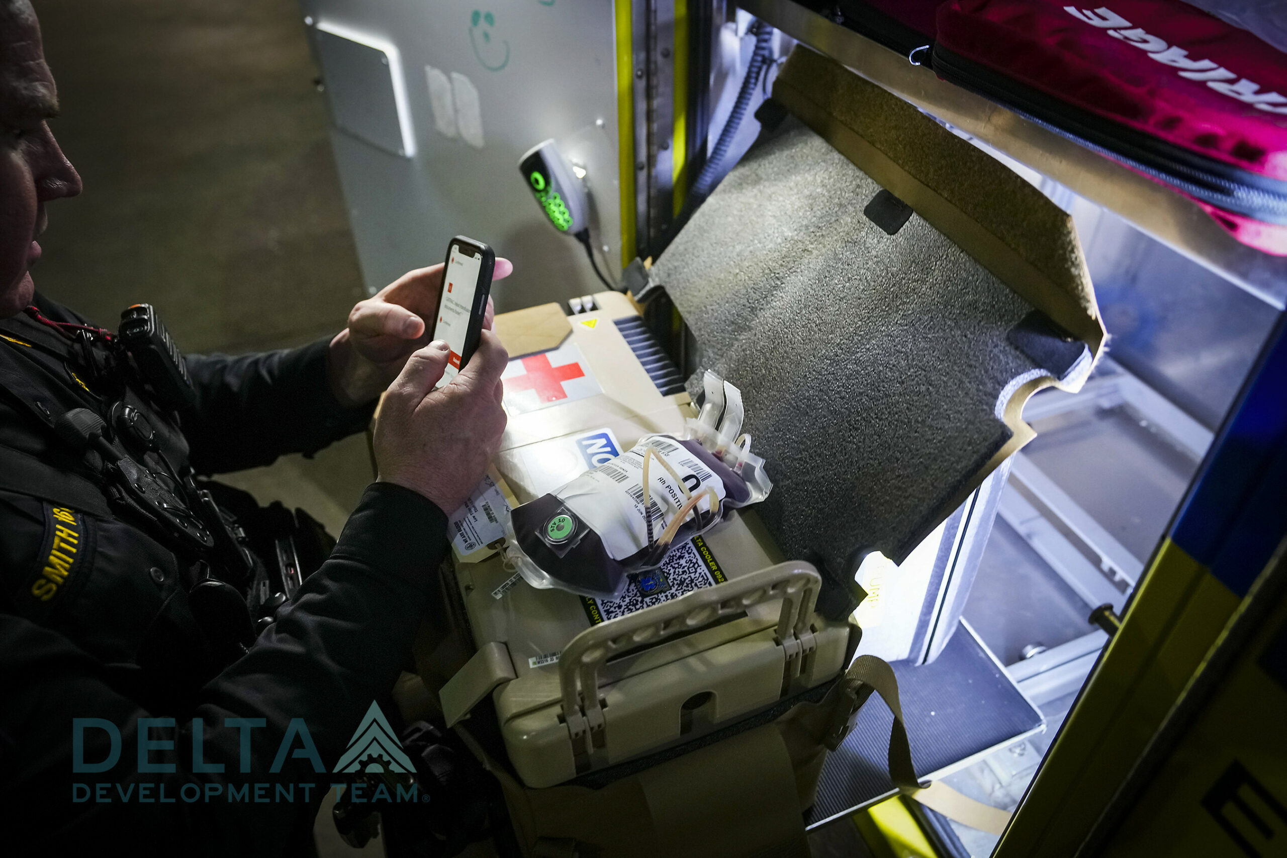 A man with an APRU on his lap with a blood bag uses his phone to connect to the device.