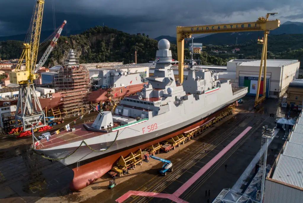 An image of the Italian Navy FREMM frigate, Emilio Bianchi, at the Riva Trigoso integrated shipyard. The ship, painted gray, is decorated with ribbons of laurels on the railings of its deck. It has "F 589" painted on its right side in red.