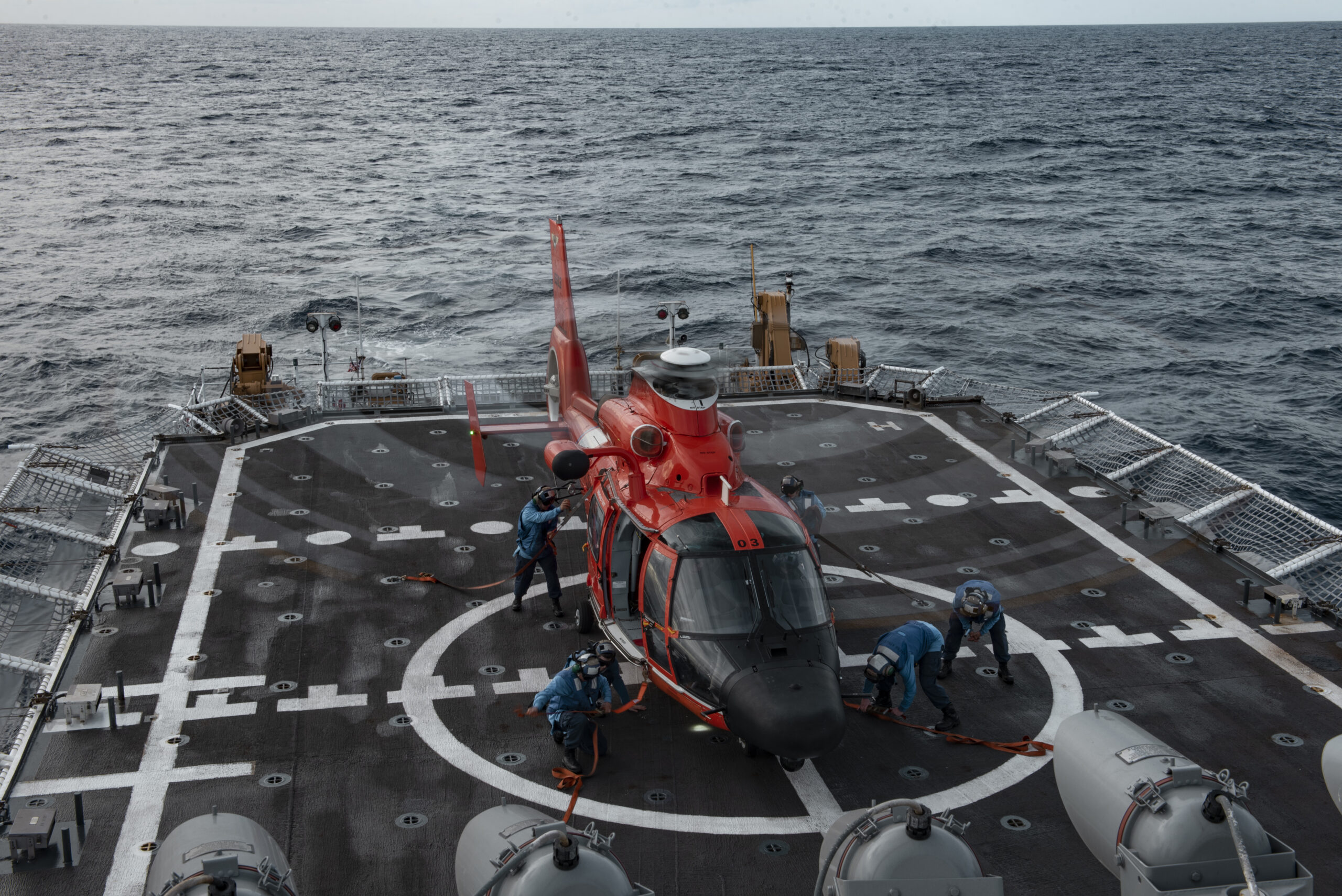 Coast Guard members aboard the USCGC Stratton (WMSL 752) conduct tie-down operations with a MH-65E Dolphin helicopter in the Pacific Ocean, Dec. 29, 2021. The Stratton crew conducted flight operations to maintain operational capabilities and increase readiness. (U.S. Coast Guard photo by U.S. Marine Corps Sgt. Sarah Stegall)