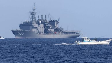 A JMSDF minesweeper vessel and two fishing boats sailing on a blue ocean