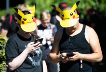 Two German adults wearing Pikachu sun visors play Pokemon GO on their phones in a park