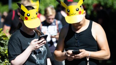 Two German adults wearing Pikachu sun visors play Pokemon GO on their phones in a park