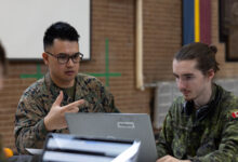 U.S. Marine Corps Cpl. Miles Young (left), data systems administrator, Defensive Cyberspace Operations, Company A, 6th Communication Battalion, Marine Forces Reserve, discusses his network hacking plan with a Canadian Army service member during Cyber Harmony 24 at The Royal Montreal Regiment, Quebec, Canada, April 28, 2024. This exercise allowed Reserve Marines to integrate with their active duty counterparts and joint partners to help develop practices in defense against cyber attacks.