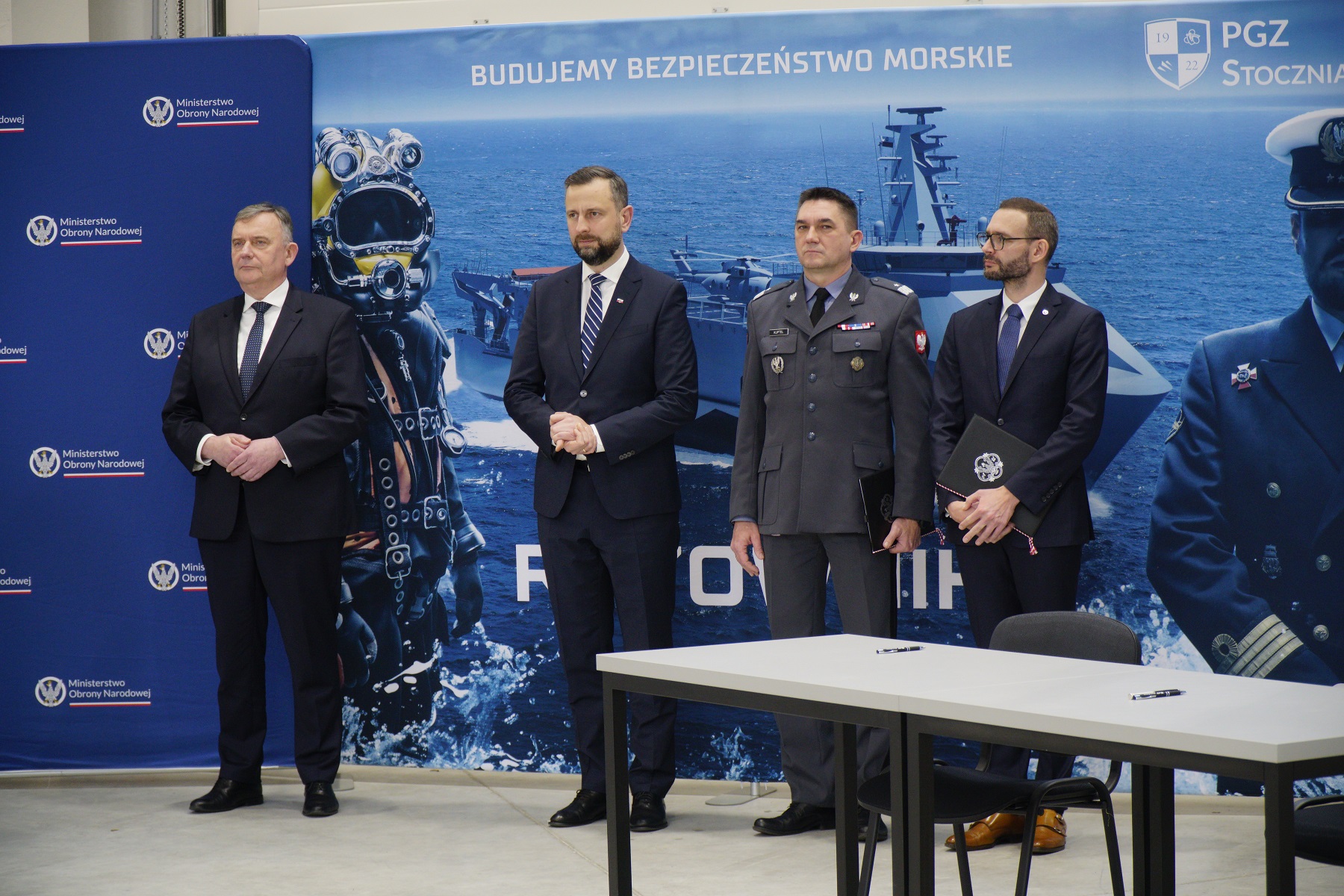 Polish defense ministry and industry leaders standing in front of the Polish Navy's Ratownik rescue ship concept design