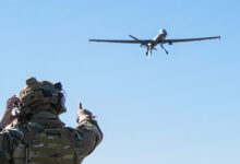 A US Air Force Airman assigned to the 1st Special Operations Support Squadron Mission Sustainment Team watches as an MQ-9 Reaper prepares to land on an unprepared dirt surface