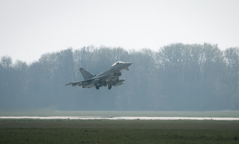 A UK Royal Air Force Typhoon jet takes off. The aircraft is colored gray, with 350 painted on its rudder. The background, partially covered in fog, appears to be a forested area.