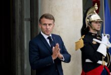 French President Emmanuel Macron rubbing his hands with a royal guard in the backgorund