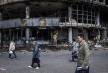 People are walking in front of a destroyed shopping mall in Liukanivka district in Kyiv.